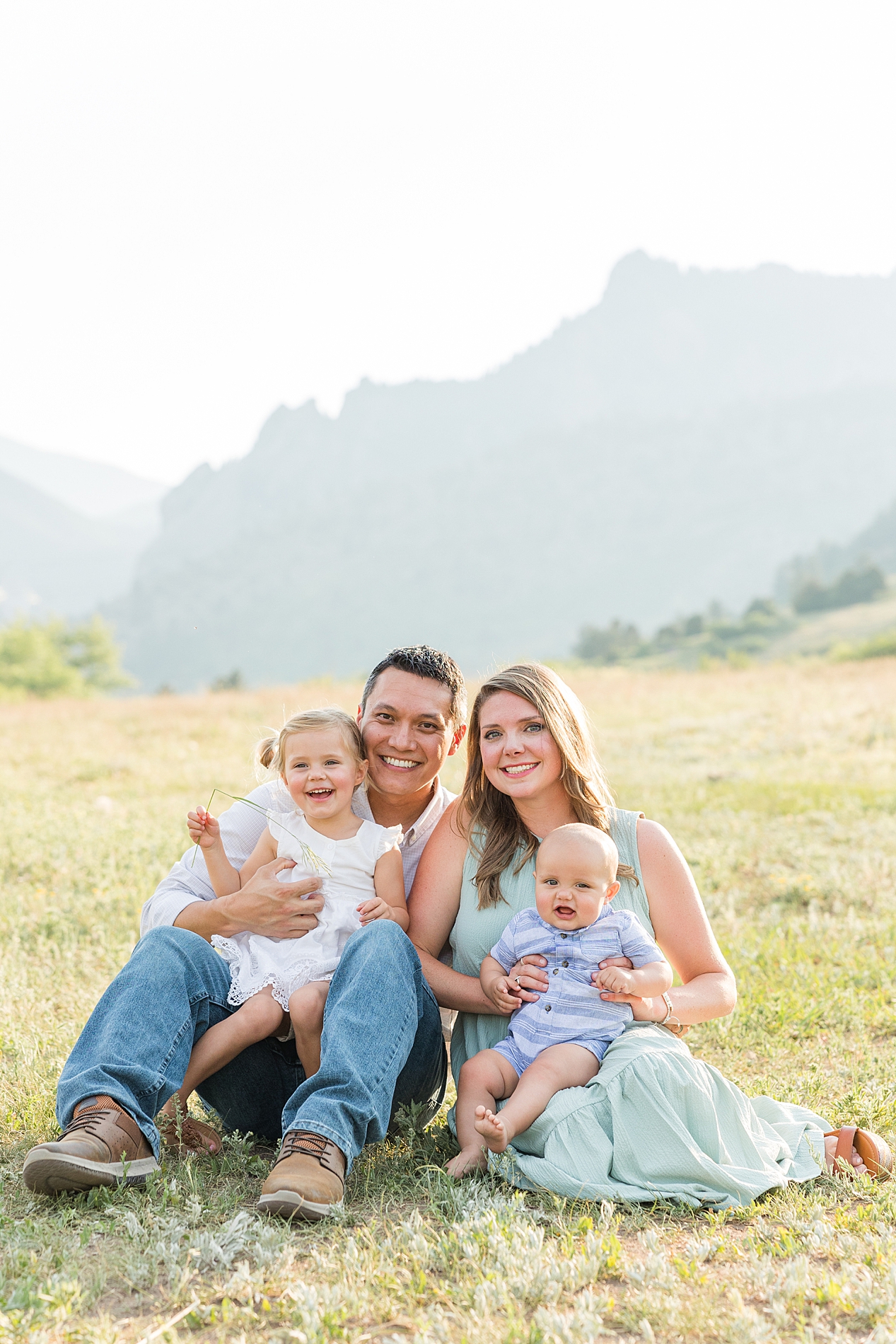 family of four sit in the grass with mountains in the background