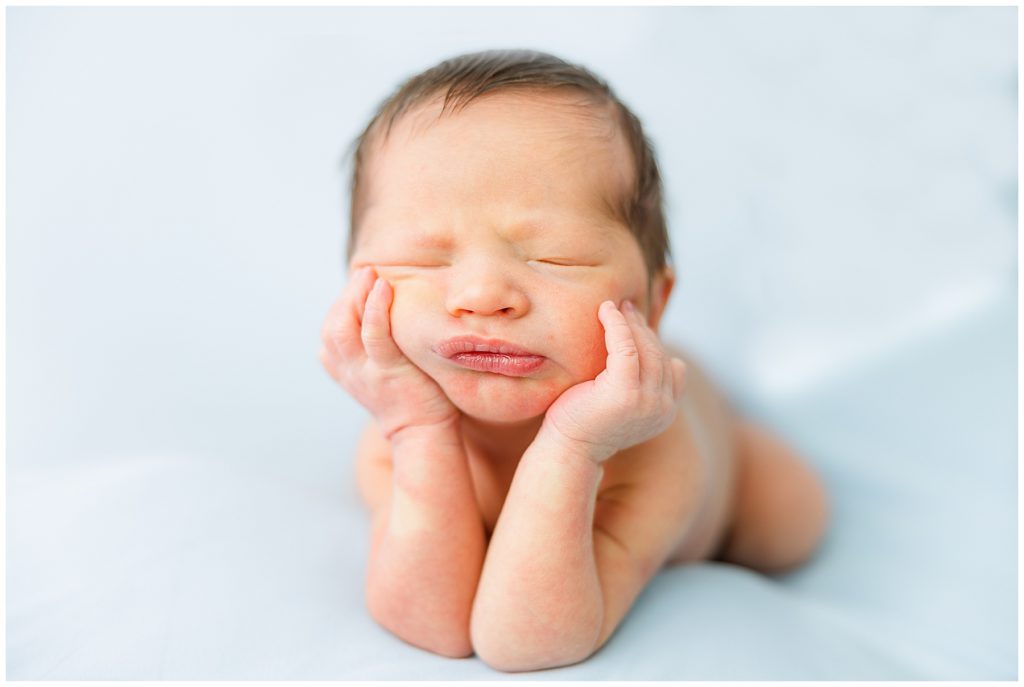 newborn propped up with hands on cheeks