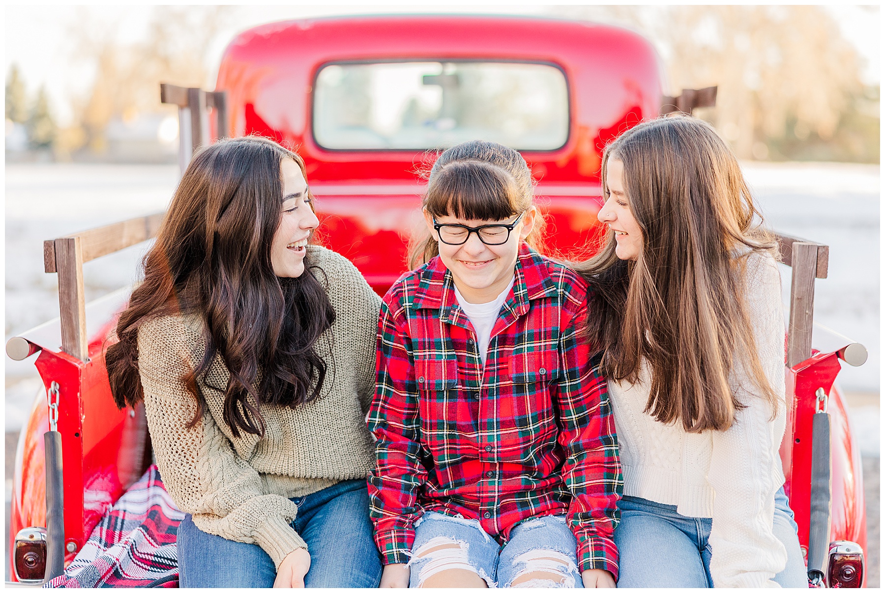 three sisters sit a giggle on the back of the tailgate of a red truck during mini session in Louisville CO