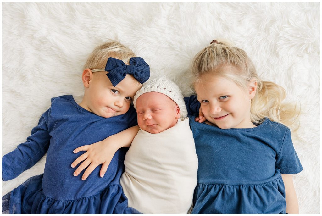 two big sisters lay with their newborn brother for lifestyle session in Aurora, CO