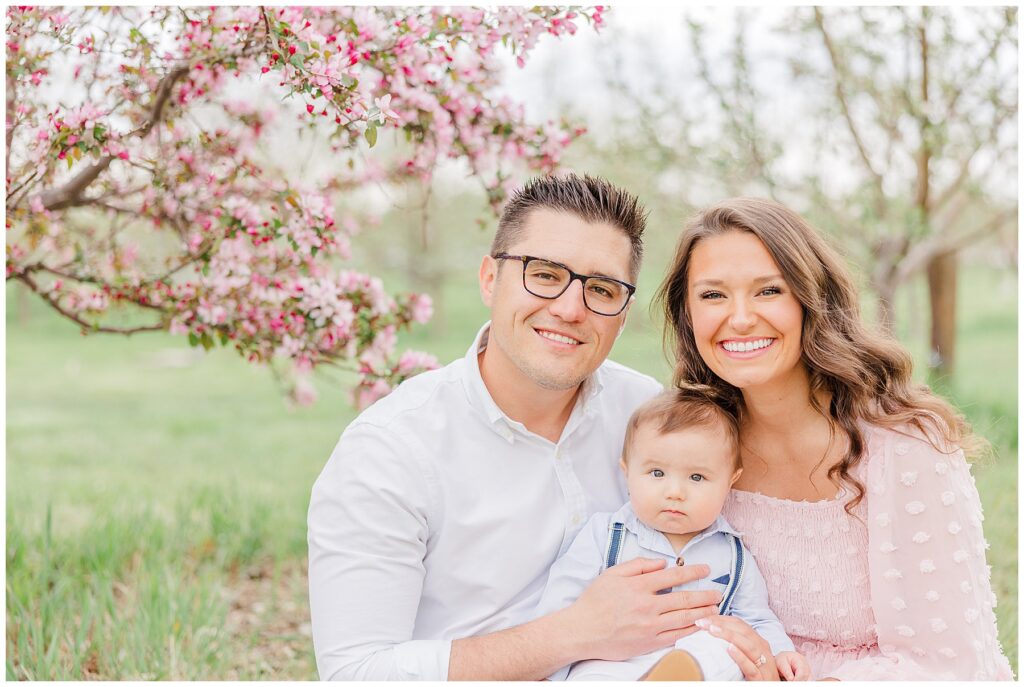 Young couple sit together holding their baby boy during outdoor spring mini sessions