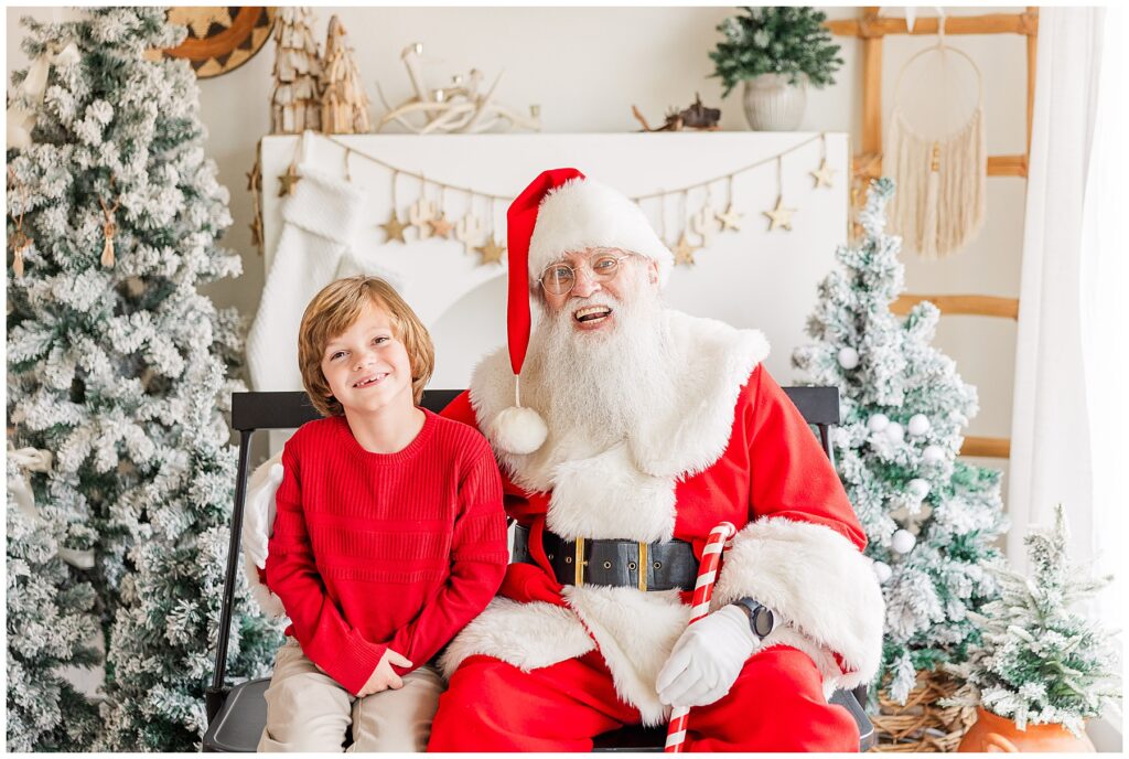 Boy in red Christmas sweater poses with Santa for light and airy studio photos in Colorado