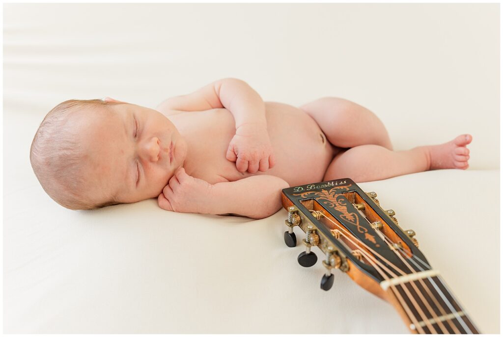 Newborn sleeps on a white background with a guitar handle in the shot