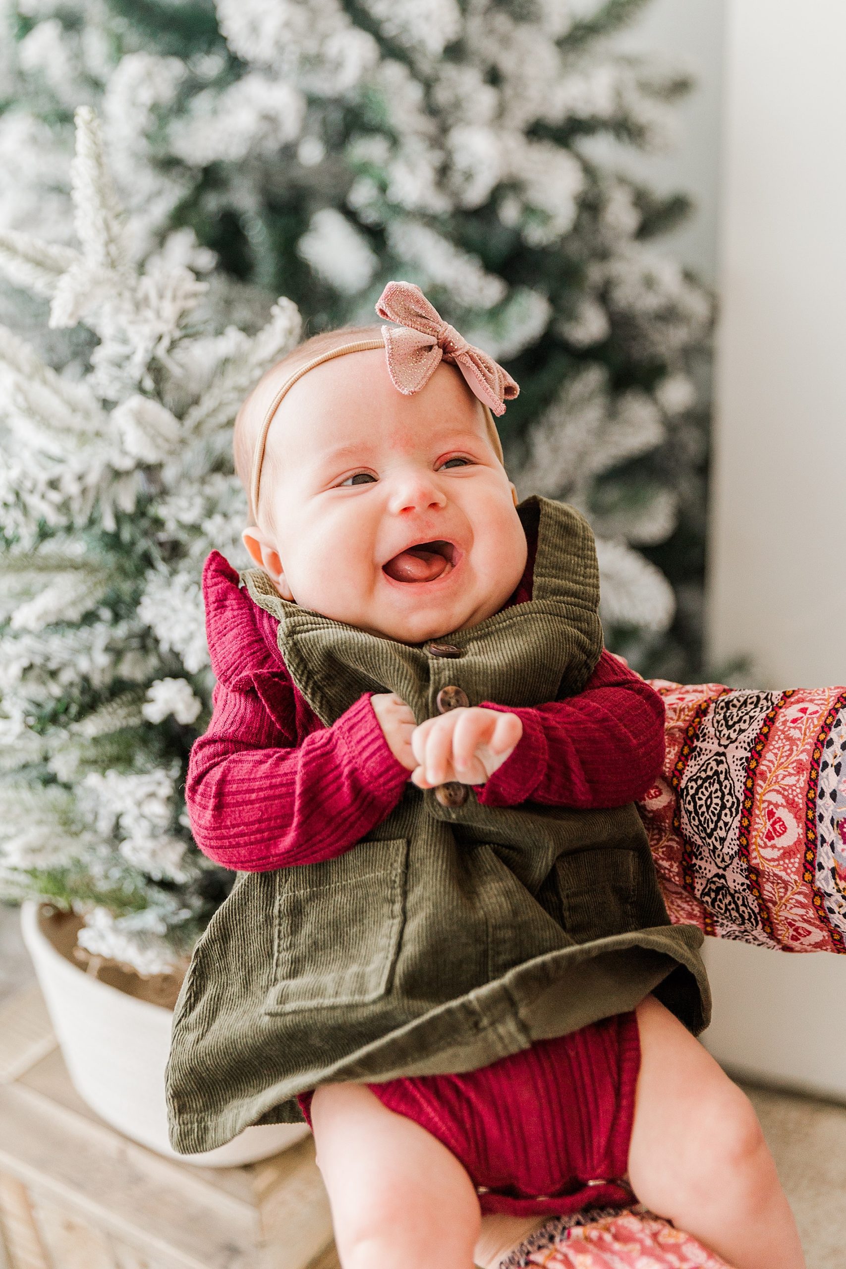 newborn girl smiles big with Christmas tree in the background