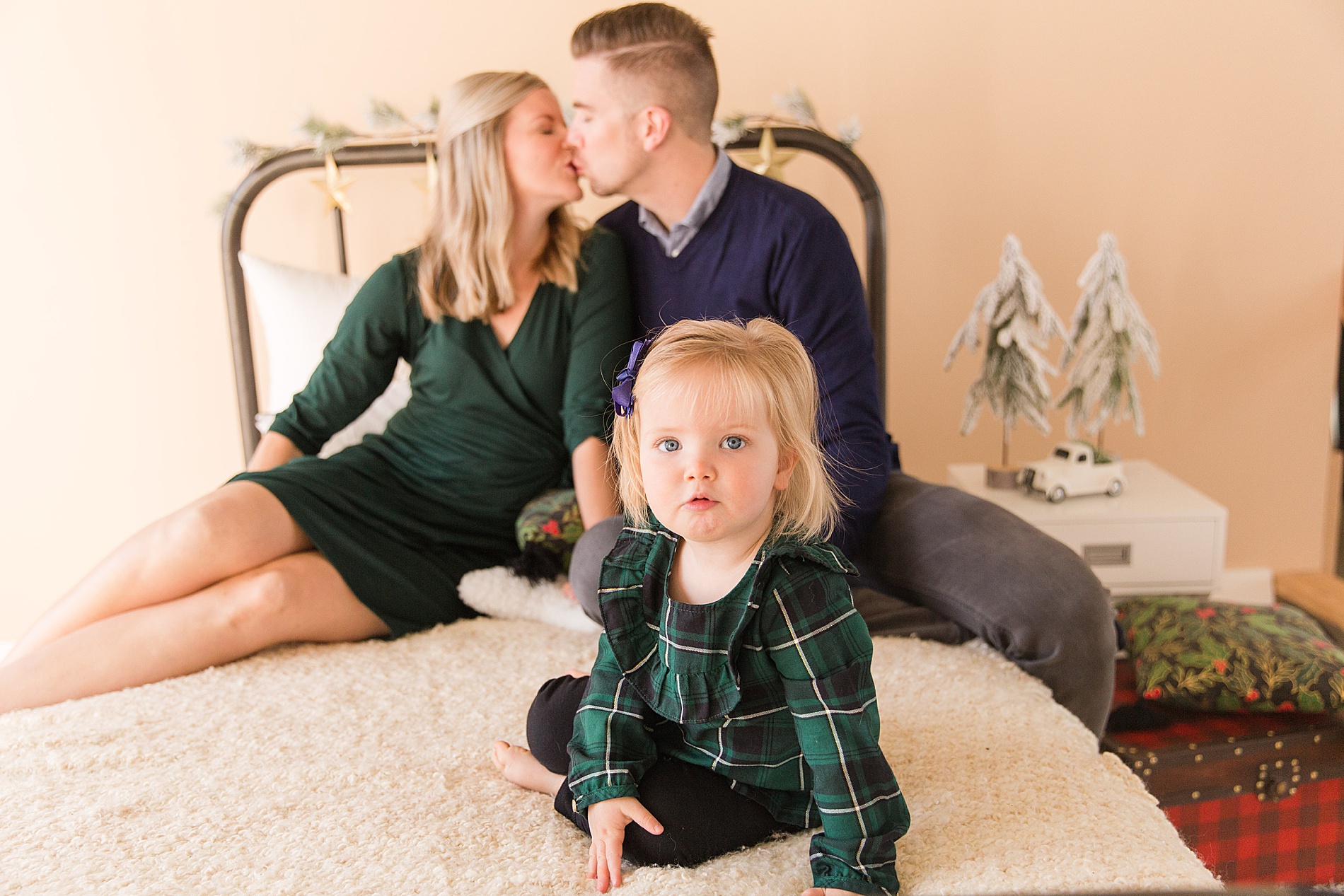 mom and dad kiss during Christmas mini session while daughter sits between them