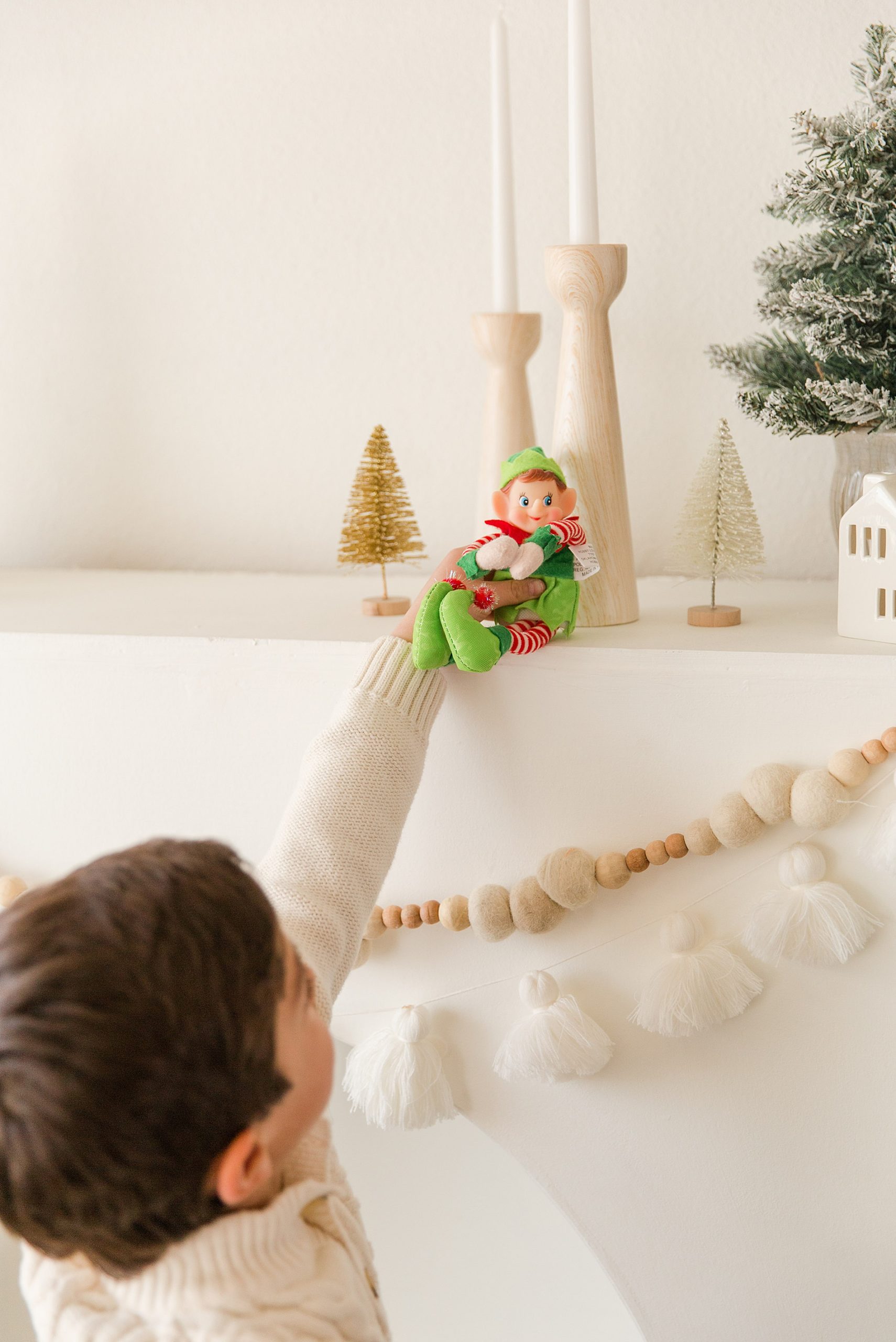 little boy places green elf on the shelf of the fireplace