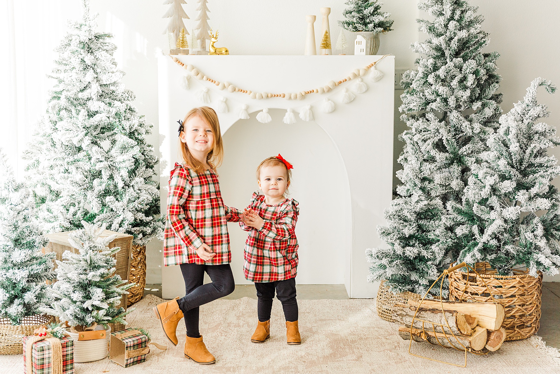 sisters in matching outfits stand near a beautifully decorated mantle for Christmas
