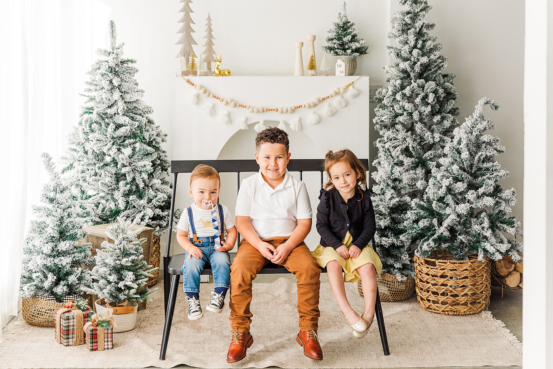 three siblings sit on a bench with a Christmas backdrop