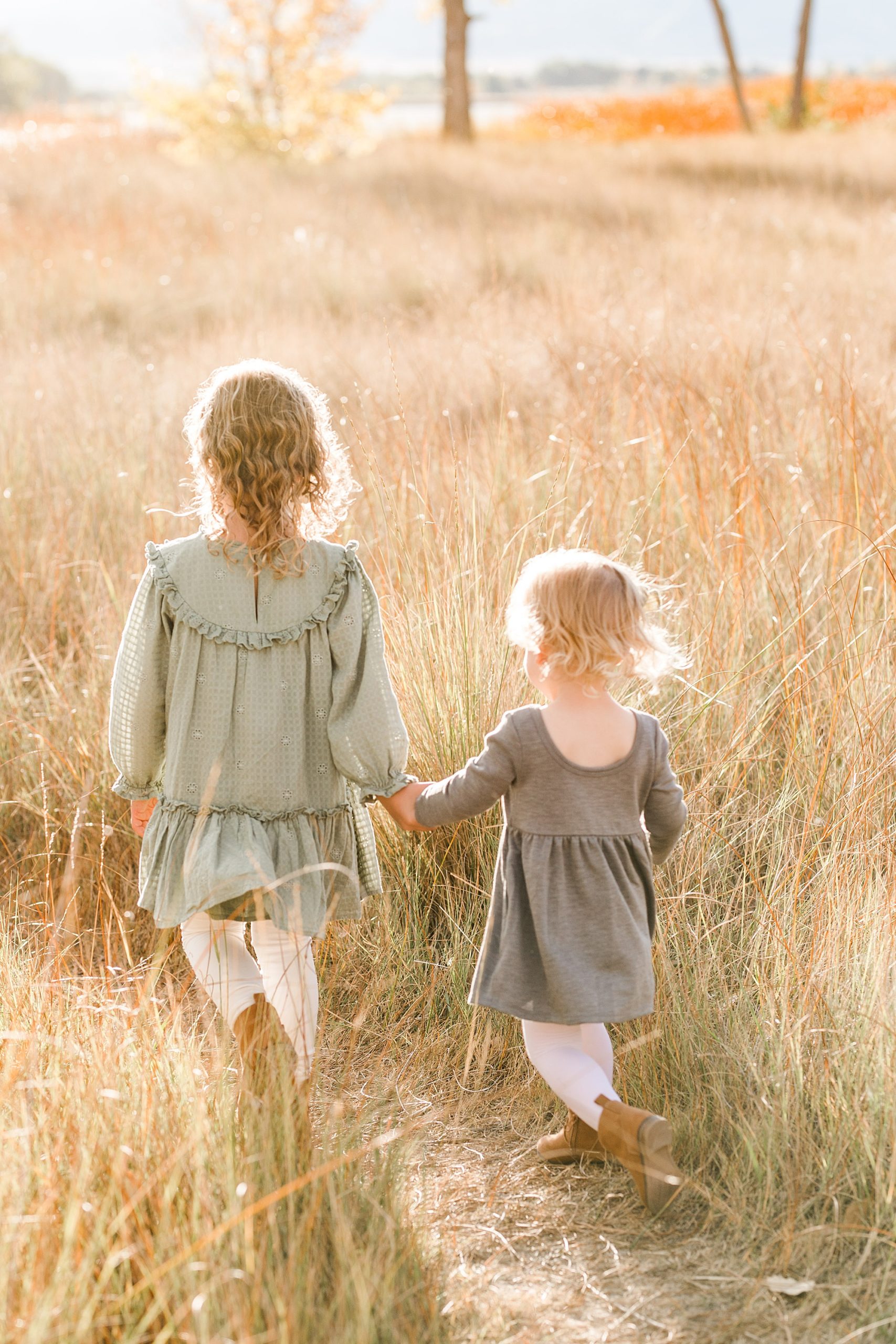 sisters hold hands and walk through the tall grass at McIntosh Lake in Longmont CO