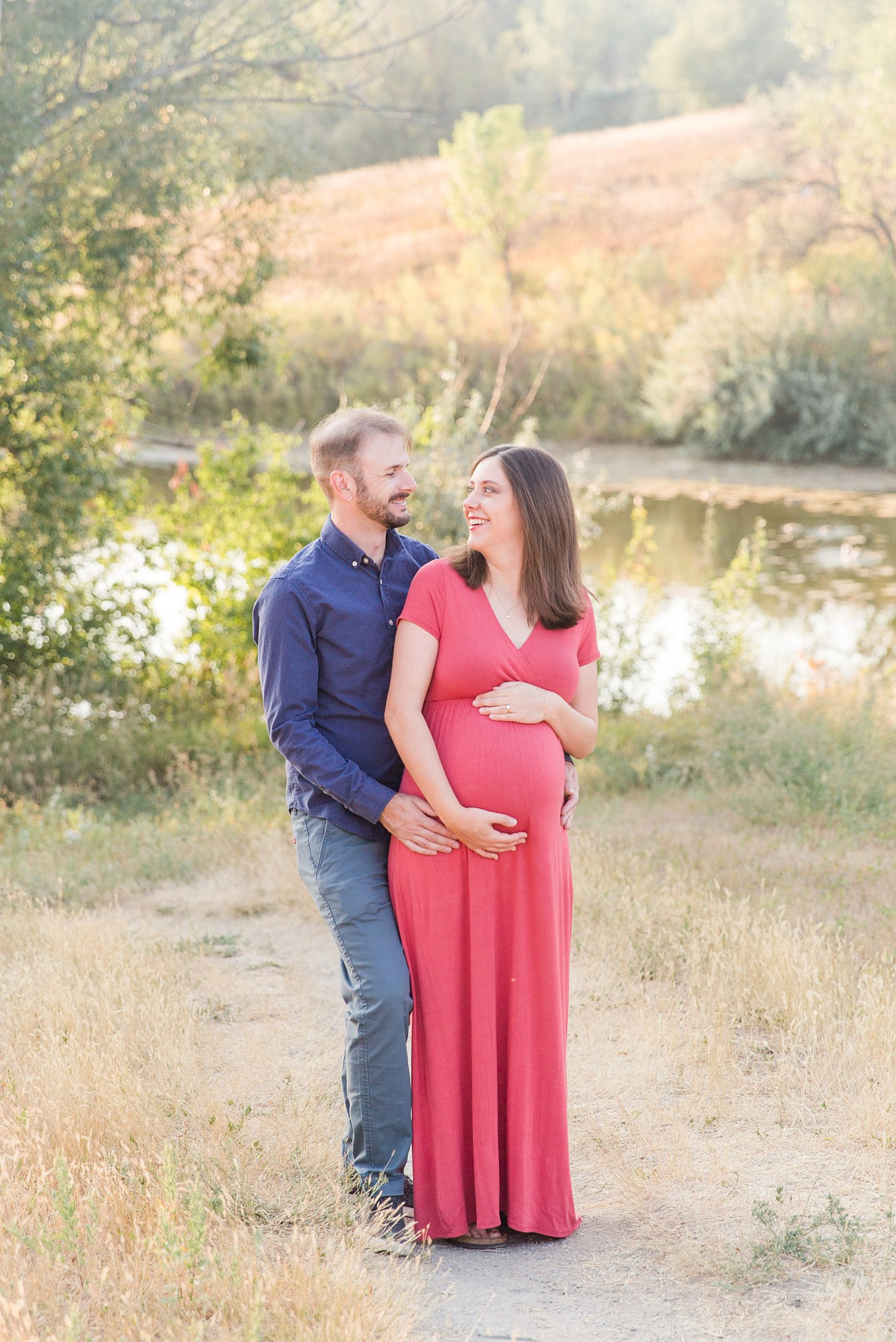 couple looks at each other while wrapping arms around baby in mom's belly during maternity session