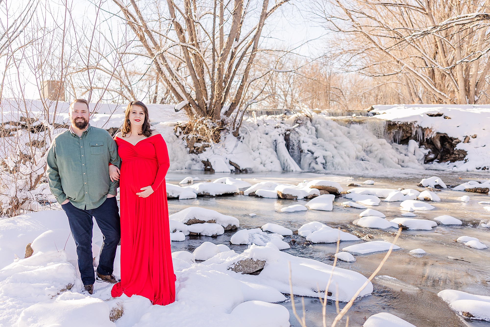 couple stands by icy pond during Golden Ponds Maternity session