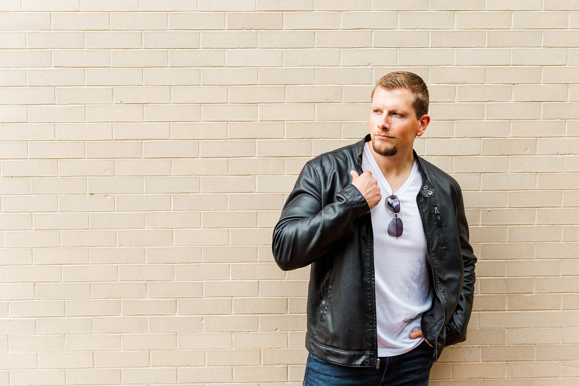 guy in leather jacket by white brick wall