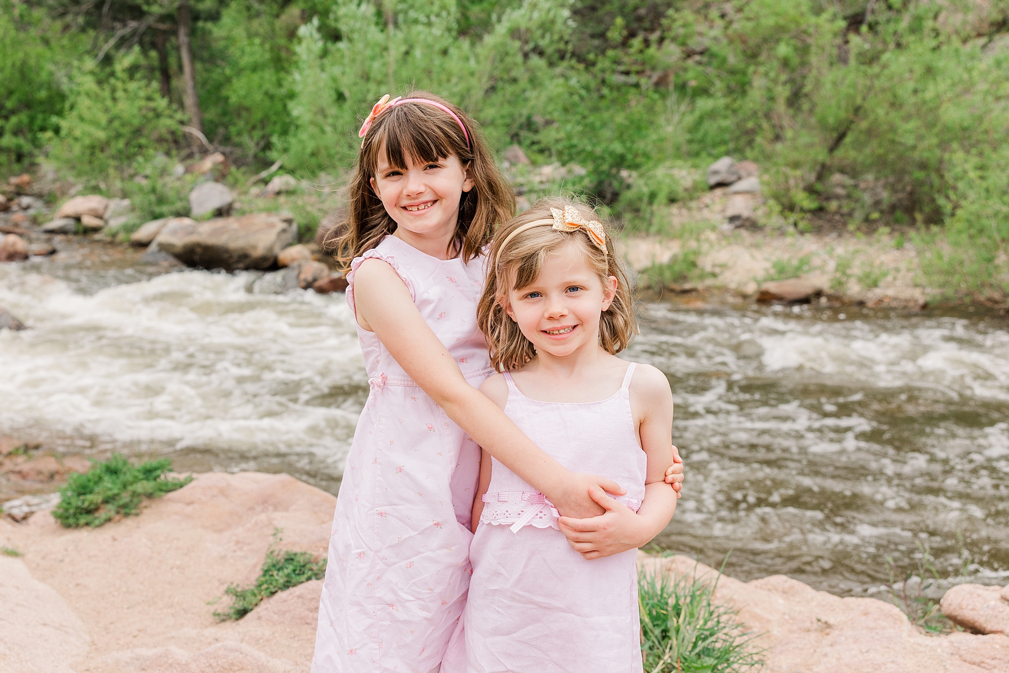 two sisters hug near creek at Buckingham Park in Boulder, CO