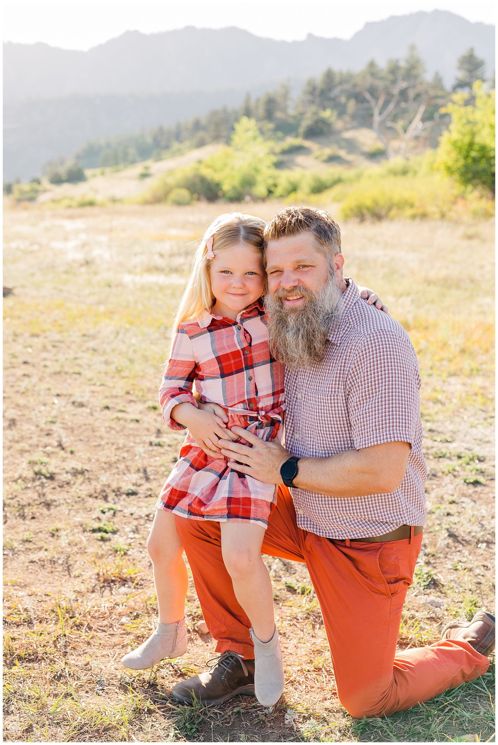 daughter sits on dad's knee in front of mountain in northern CO