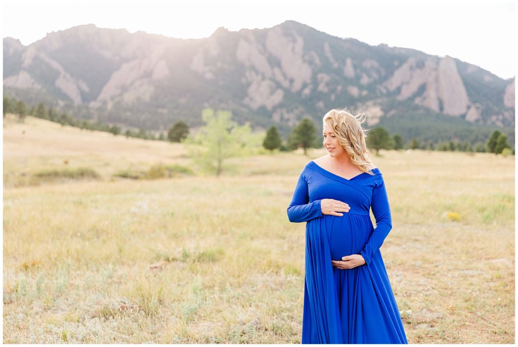 mom holds her baby bump while looking away during maternity photoshoot with flatirons in the background