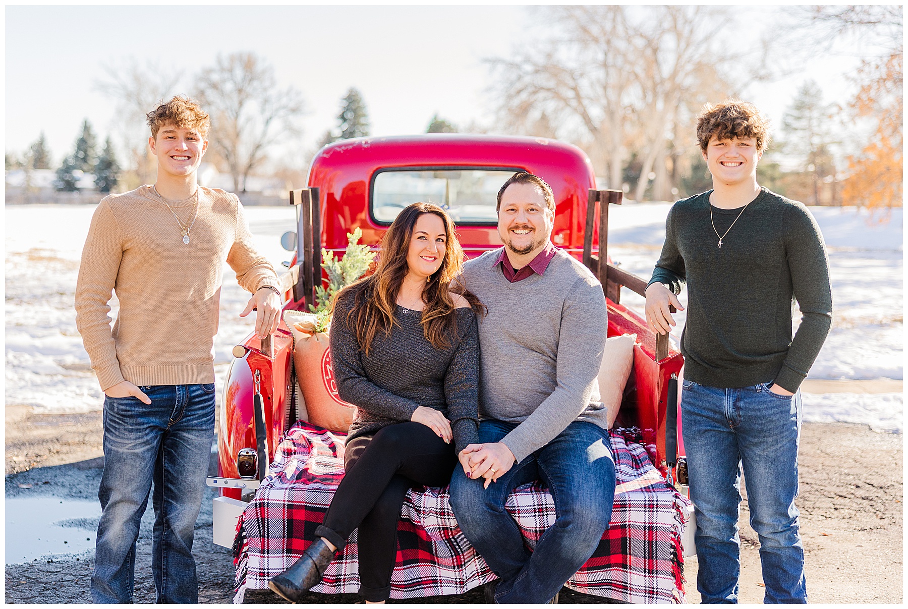 two teen boys stand on either side of the truck with their mom and dad on the tailgate