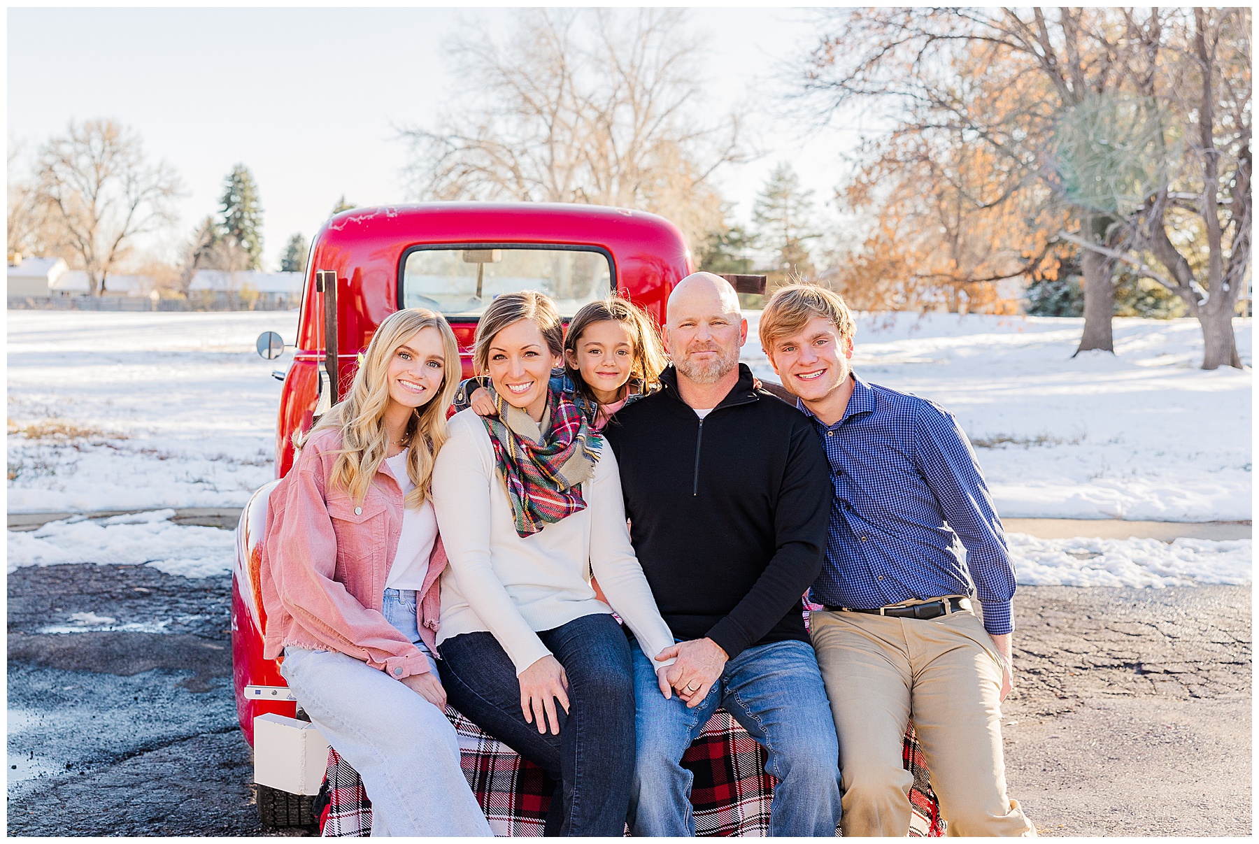 Family of five sit together on the back of a red truck during Christmas minis