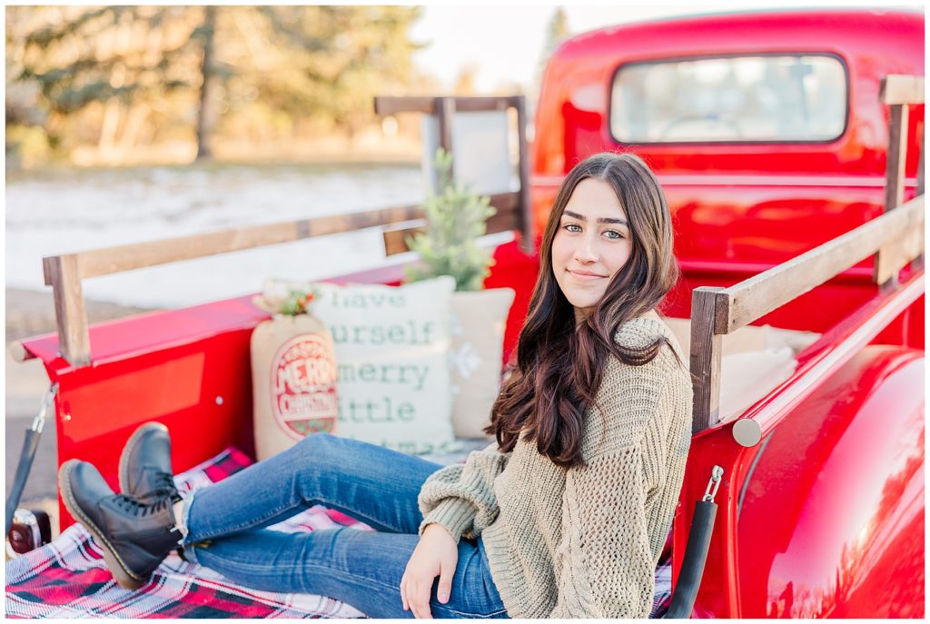 Teen sits longways on back of a tailgate during red truck Christmas minis