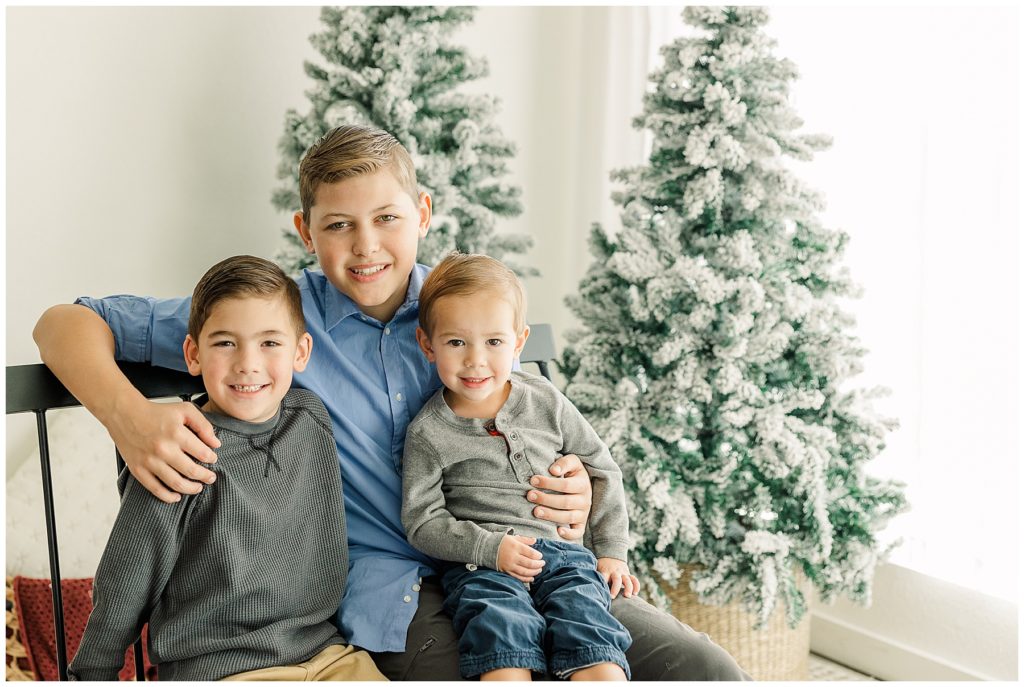 three brothers sitting in front of Christmas trees in studio for family pictures