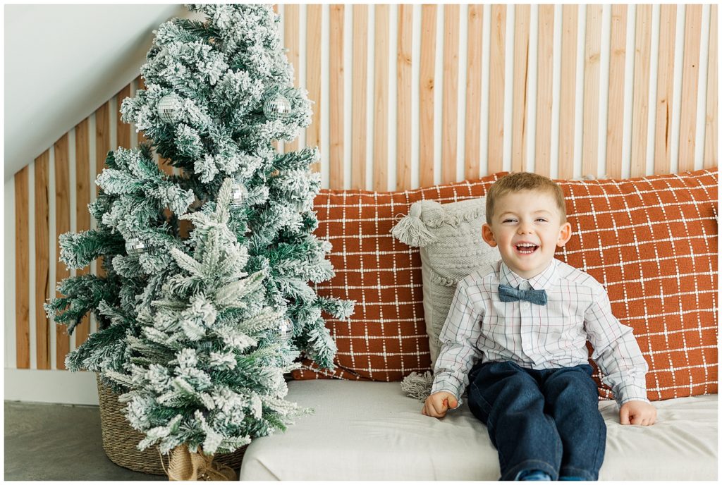 young boy in a bowtie smiles for the camera during Christmas family portraits