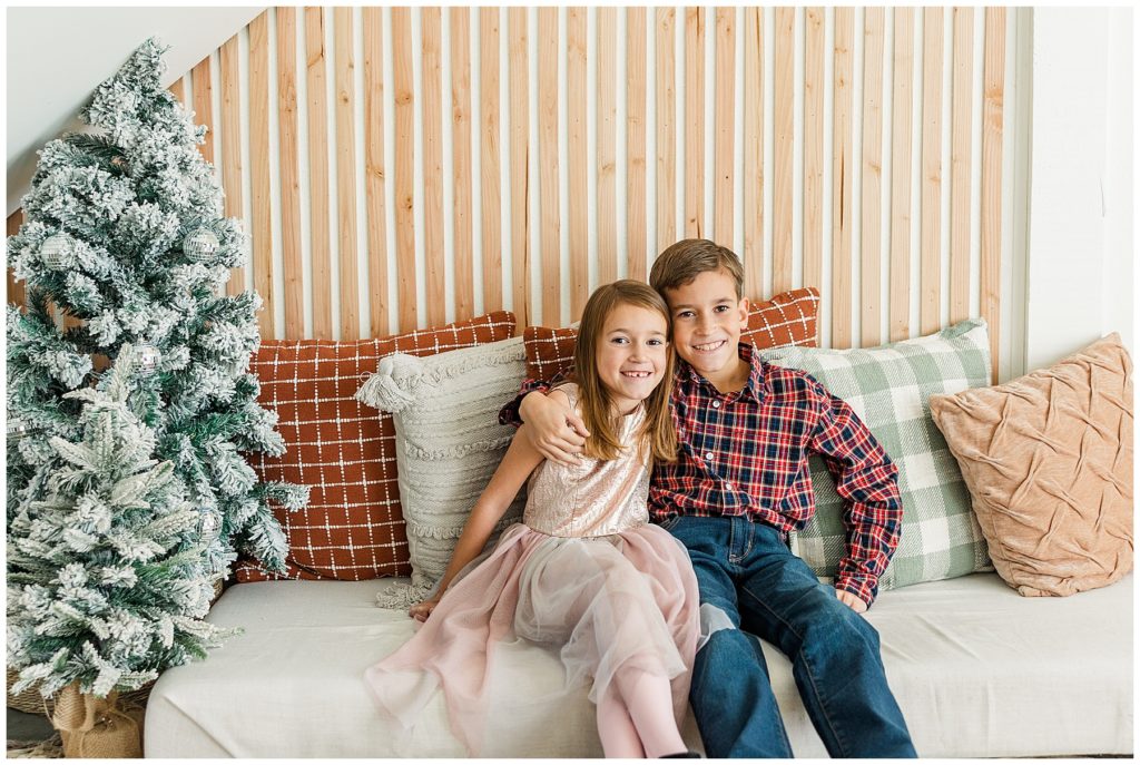 brother and sister pose with their arms around each other's shoulders during Christmas mini session