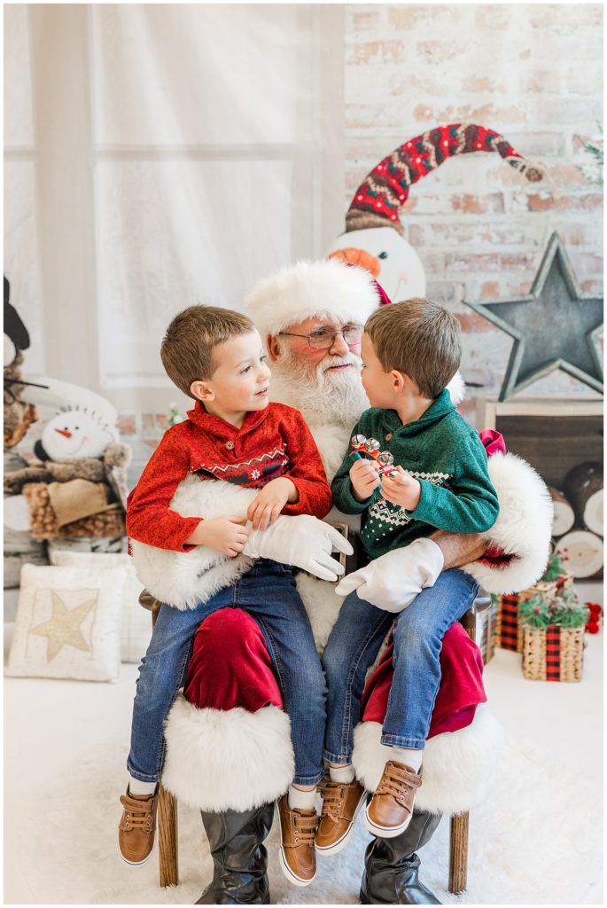 young twin boys look at Santa and each other while Catherine Chamberlain takes their photo at a Christmas social for a non-profit organization in Boulder, CO