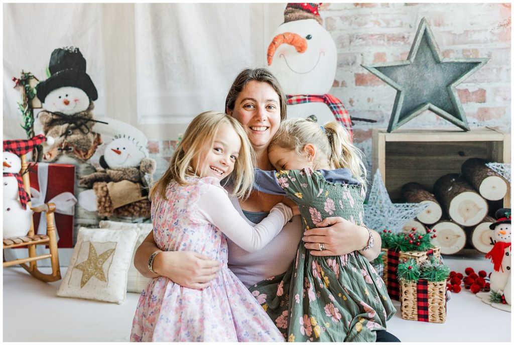 Twin girls snuggle their mom on snowman set during a Christmas social