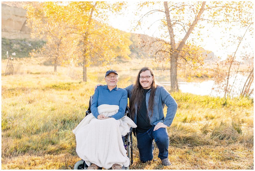 Son crouches down beside his dad who is sitting for fall family photos in Longmont, Colorado