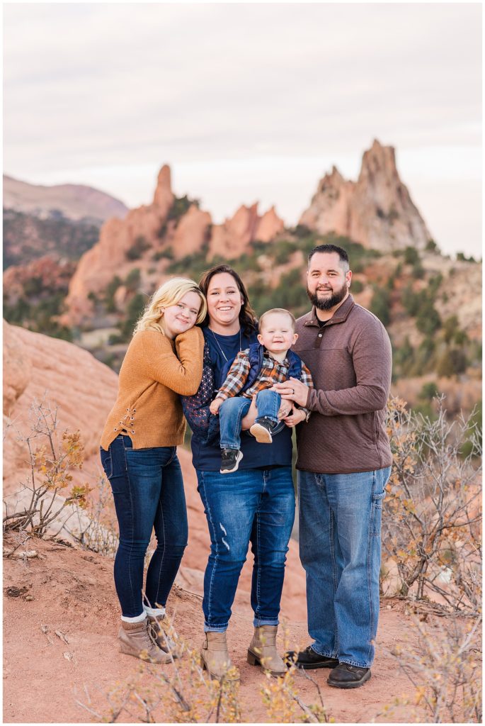 Family of four stand at Garden of the Gods with Pikes Peak in the background of family photos