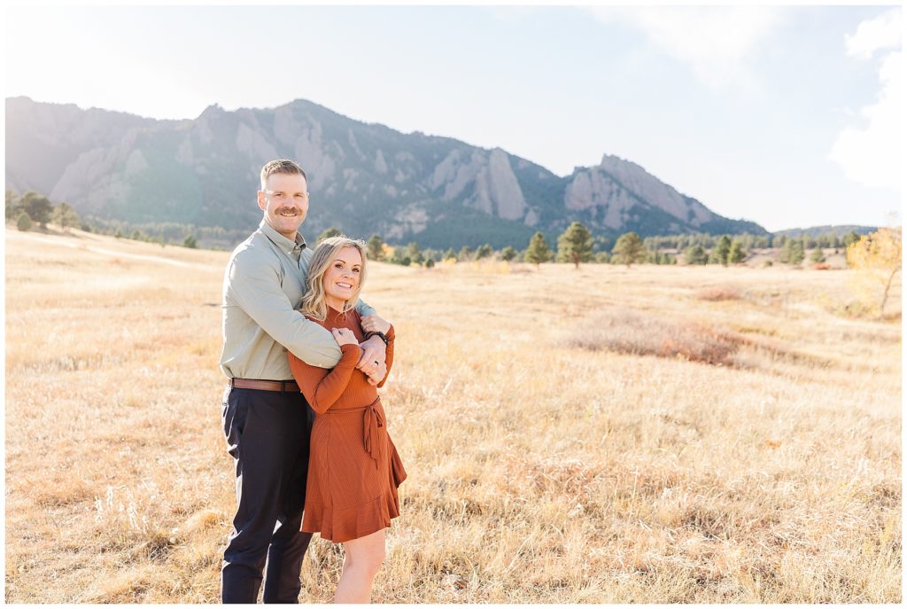 Wife crosses her arms and holds her husband's hands and he cuddles her during outdoor photography session