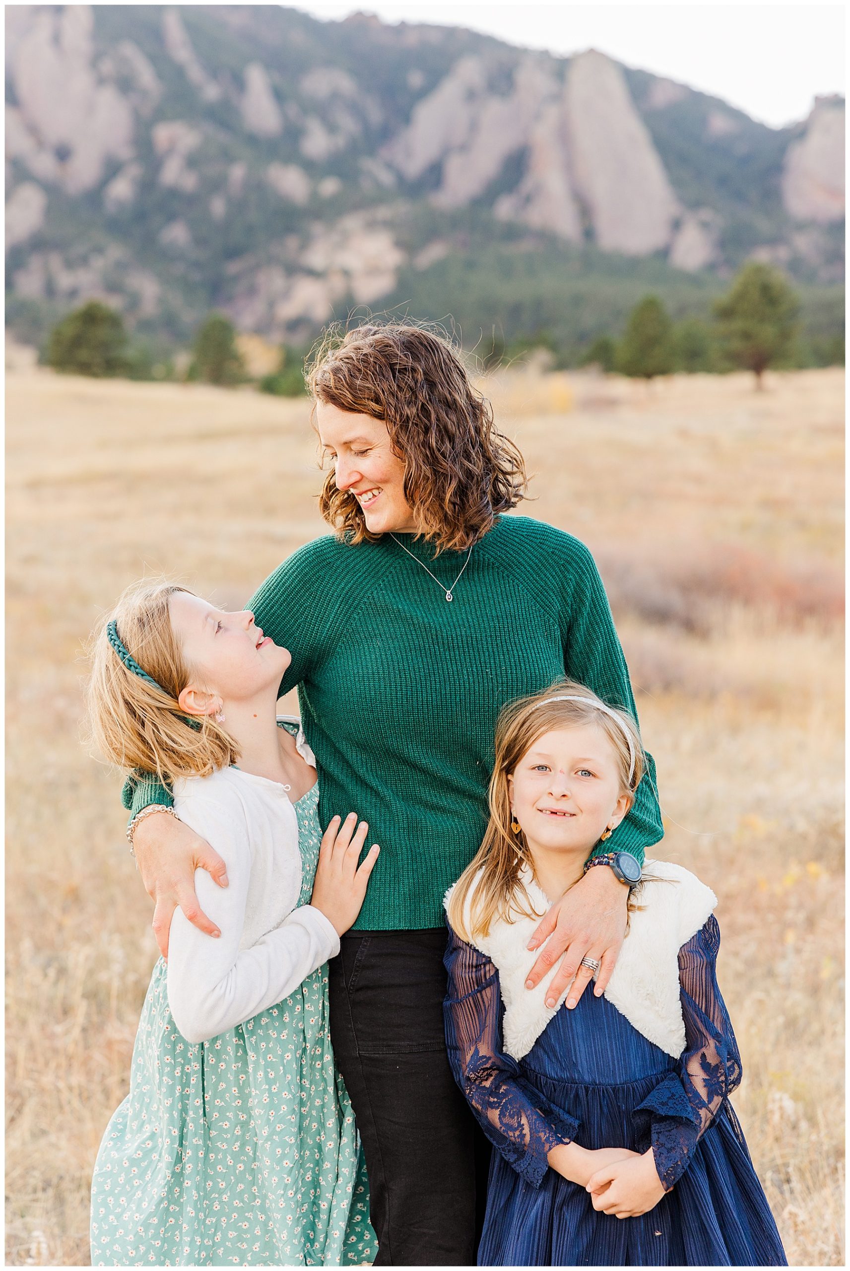 Oldest daughter looks up at her mother who has her arms around both girls in an open field in Colorado