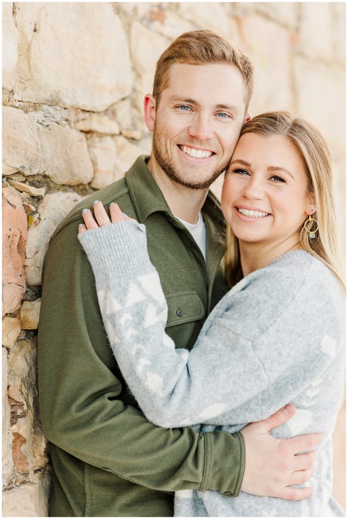 Close up pose of a couple against the wall with her hand on his shoulder and his hand on her back 