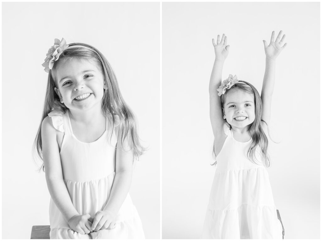 Little brunette girl poses for black and white photos with her hands raised in the air above her head