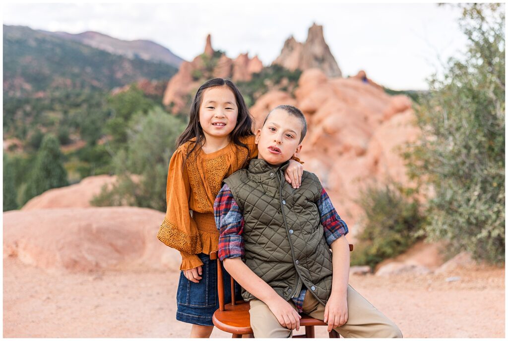 Brother sit in a chair while his sister puts his arm around him at Garden of the Gods