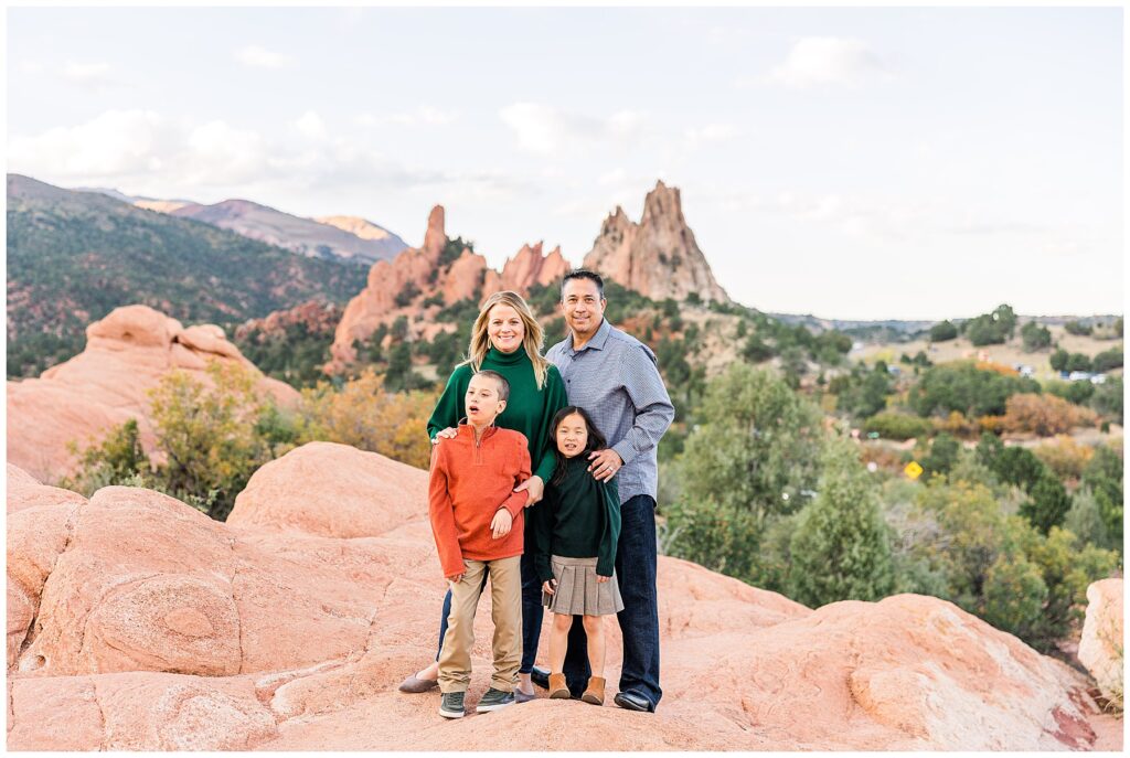 Family of four with two kids pose for spring pictures outdoors with a mountain background in Colorado