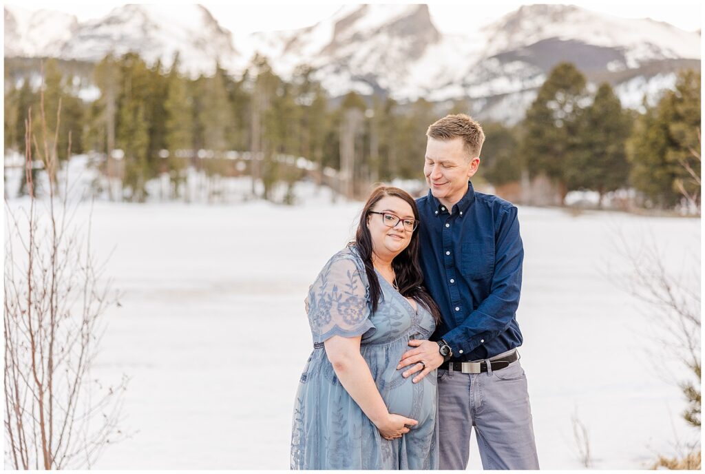 Husband and wife place their hands on expecting mother's belly at Rocky Mountain National Park 