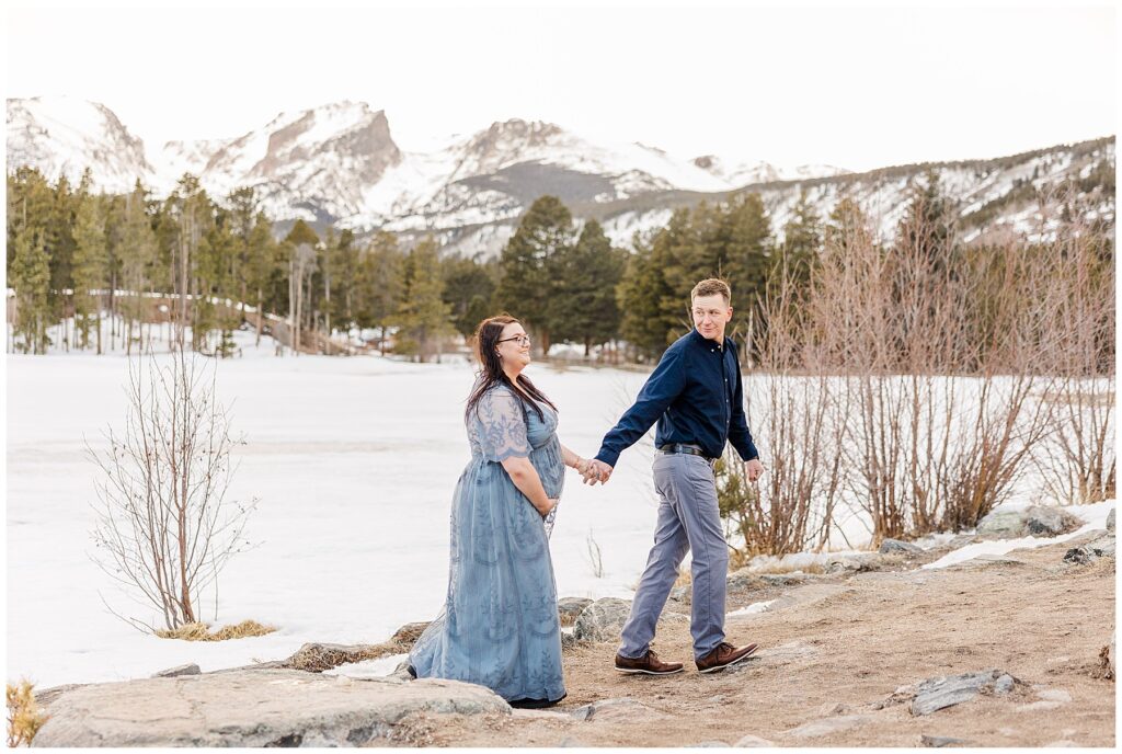 Wife places her hand on her belly while being lead by her husband who was holding her hand for light and airy photos with Catherine Chamberlain Photography for Sprague Lake Maternity shoot
