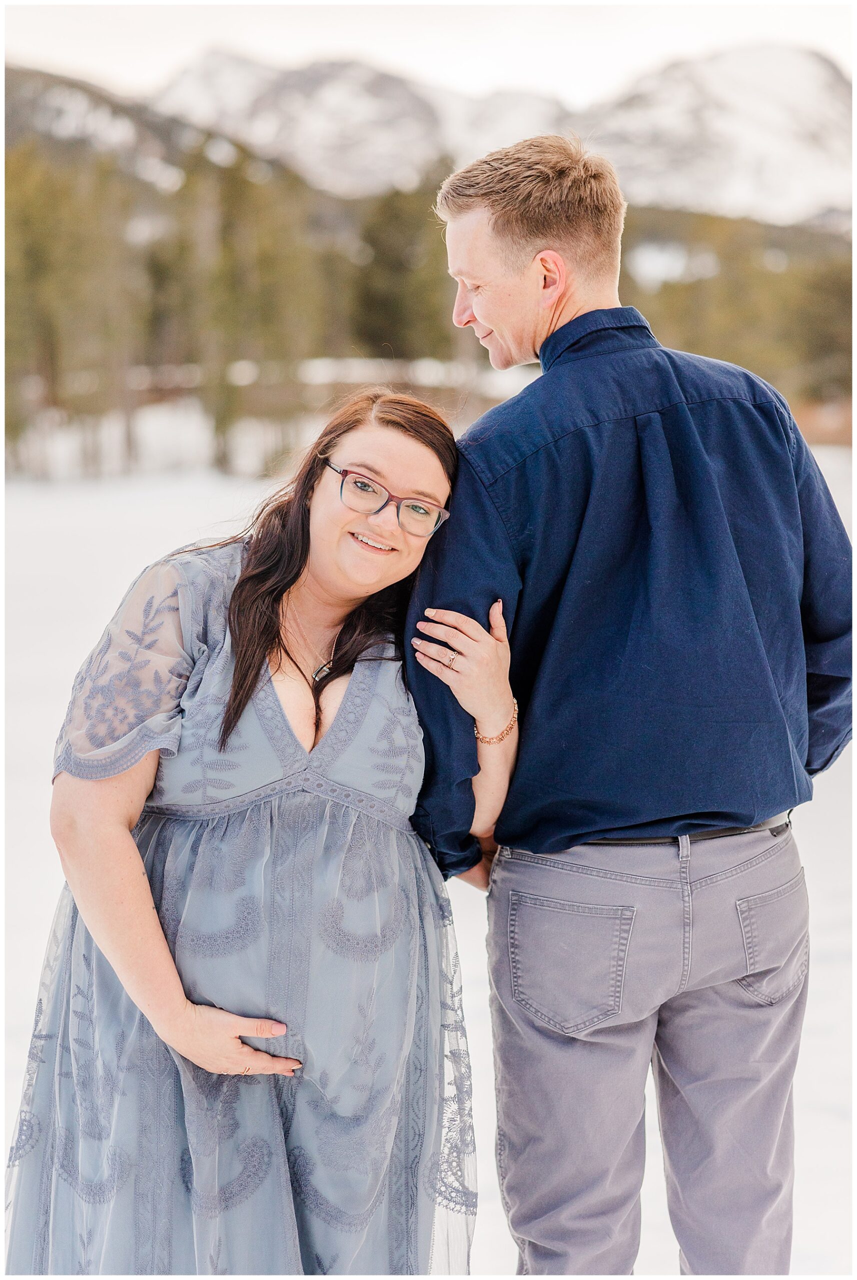 husband looks down at wife as the wife holds baby bump at maternity session Rocky Mountain National Park