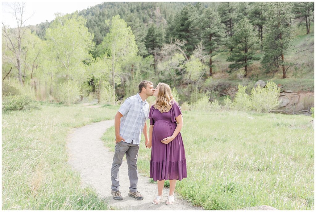 Expecting couple kiss while standing on a winding path for light and airy photos with family photographer from Northern CO Catherine Chamberlain Photography
