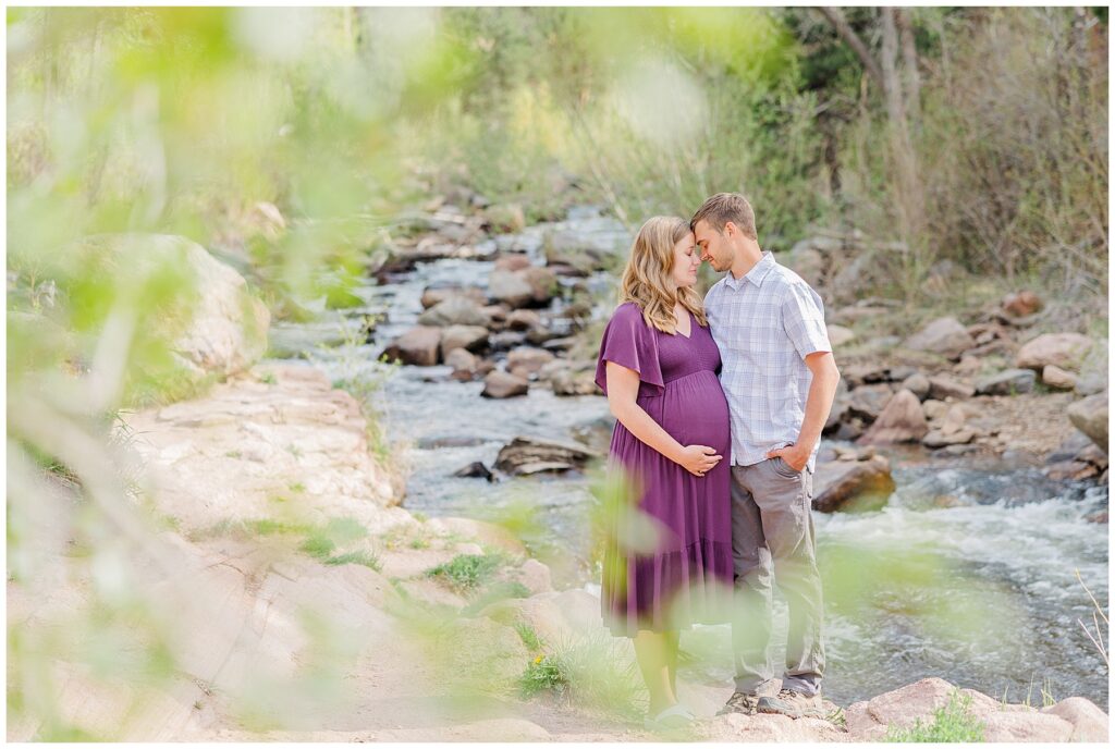 Perfectly framed picture of husband and wife posing for maternity pictures by a creek in Northern Colorado