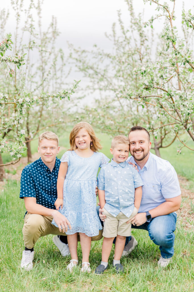 Four family members squat together for Lantzy Extended Family Session | Ya Ya Orchard in Longmont, CO