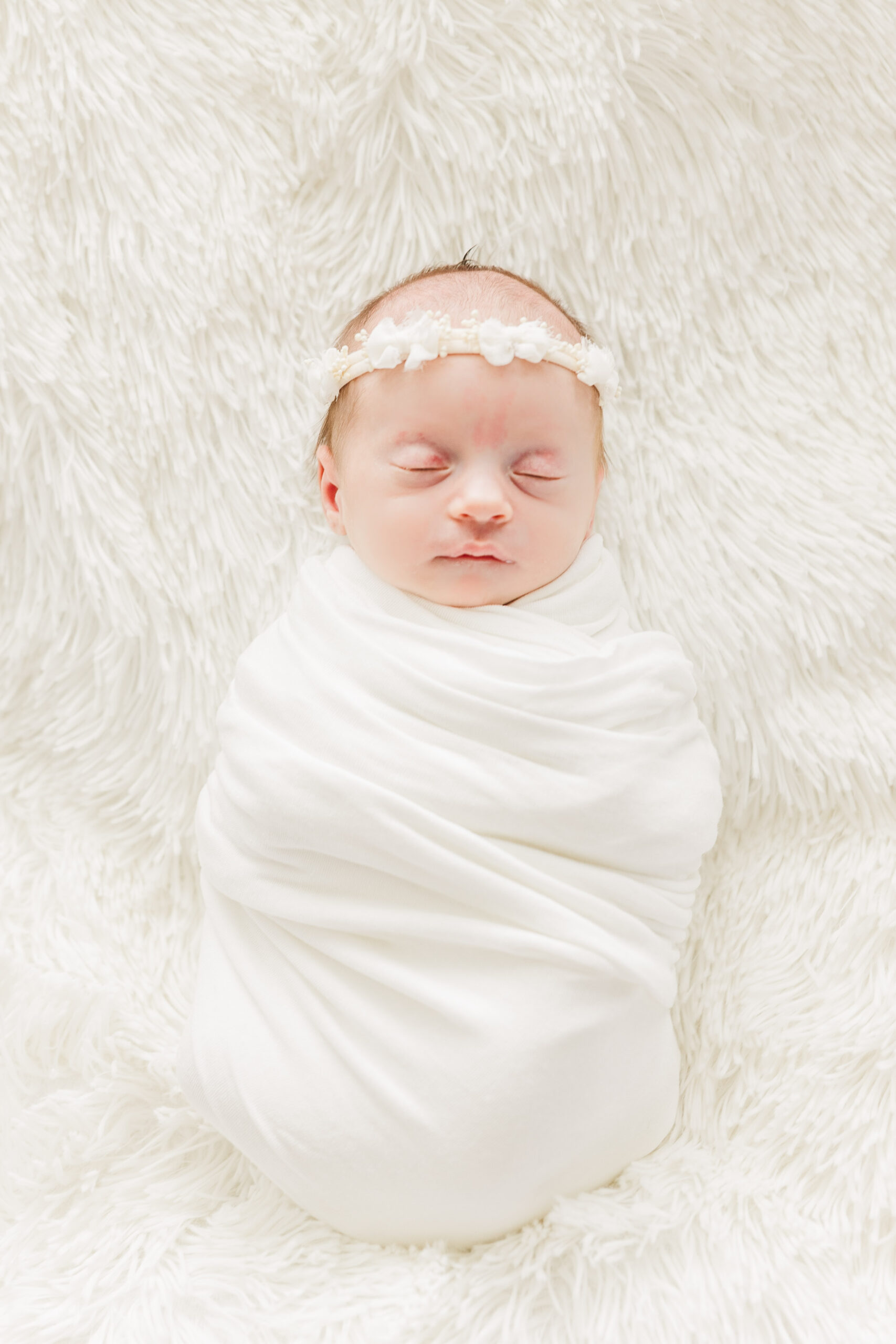Swaddled baby girl sleeping with a headband on with a white background for Conklin Family Newborn Session
