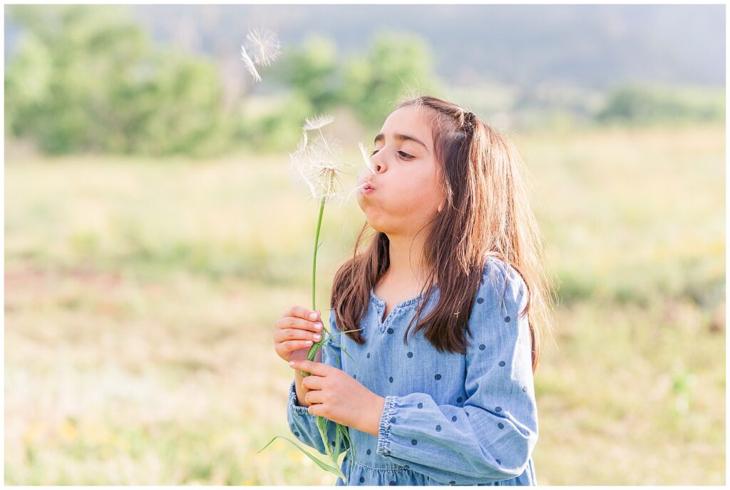 Little girl blows a dandelion during light and airy photoshoot at South Mesa Trailhead in Boulder, CO