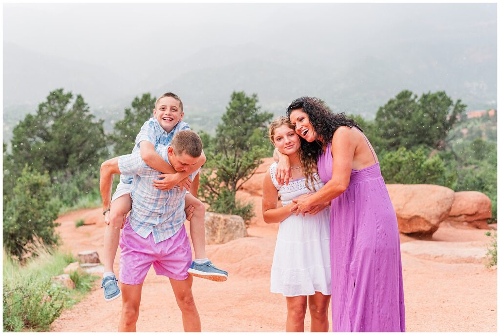 Brothers do a piggy back while mom and sister hug during family photos by Catherine Chamberlain Photography in Colorado Springs