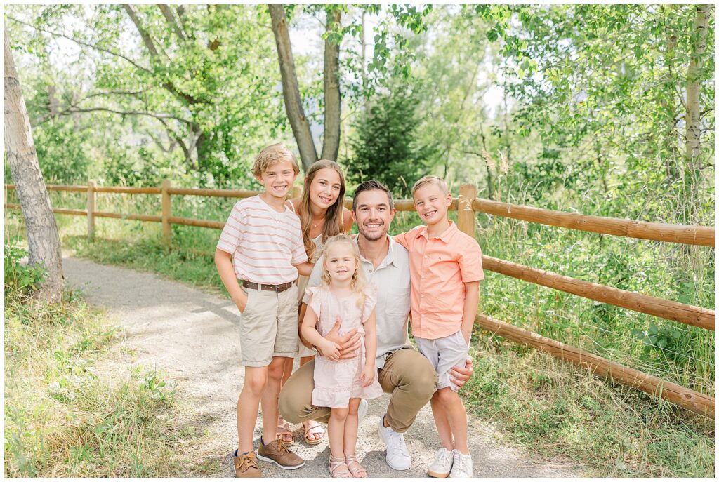 Family of five pose by a fence lined with green trees