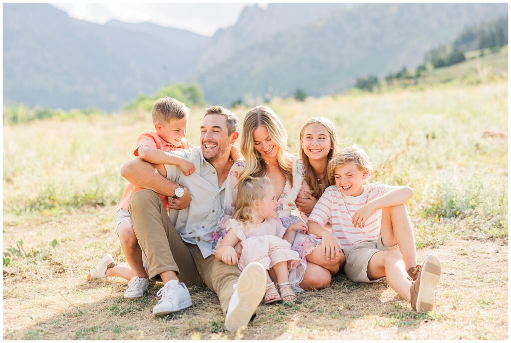 Family of six laugh and look at each other while sitting on the ground with Boulder flat irons in the background
