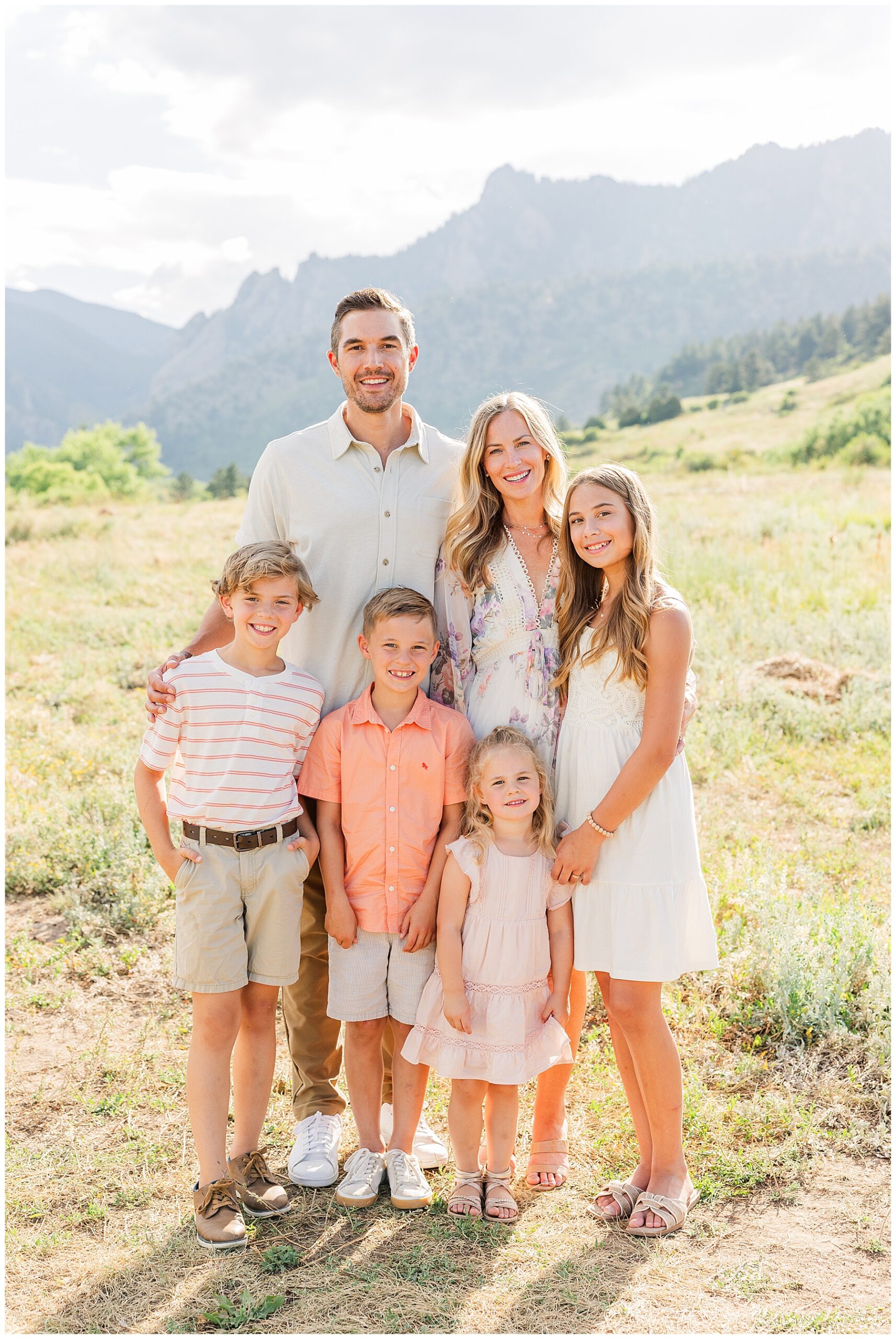 Family of six pose in an open field with the Boulder, CO flat irons in the background