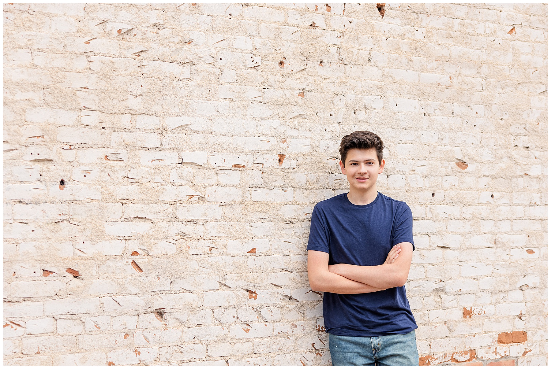 Teen boy poses for his senior pictures by leaning on a brick wall with his arms crossed while looking at the camera for Alexander’s Outdoor Senior Session in Fort Collins, CO