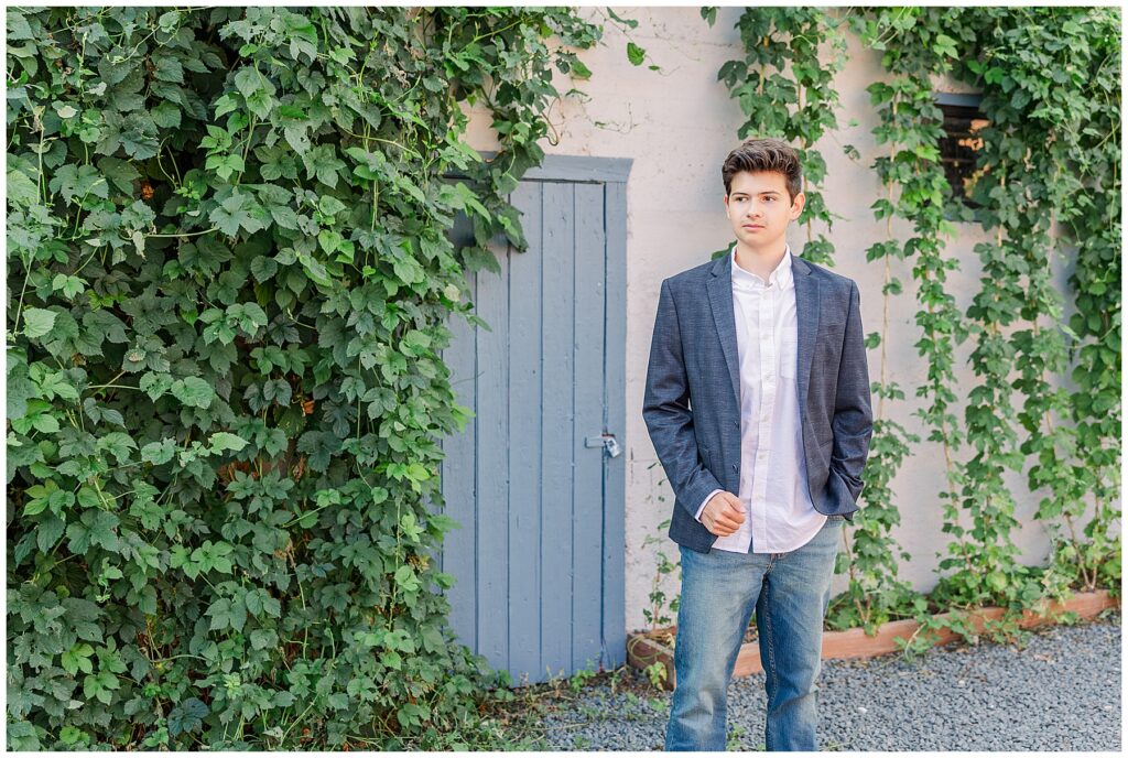 Teen stands in front of a door covered in greenery with a hand in his pocket