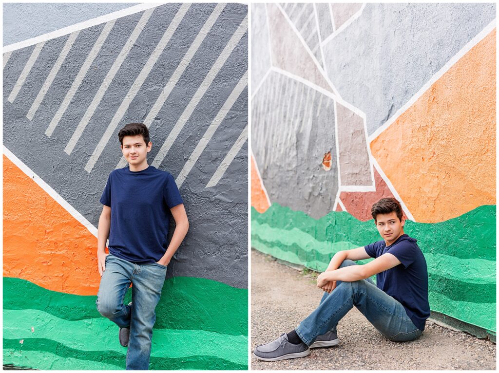 Teen poses for senior pictures by sitting on the ground in front of a wall mural